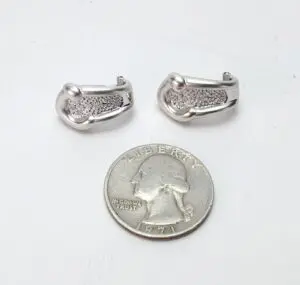 Silver earrings beside a quarter coin.
