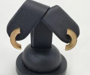 Gold crescent-shaped earrings on black stand.
