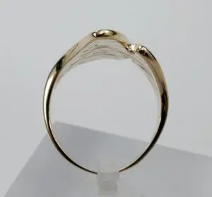 Gold ring displayed on a white stand.