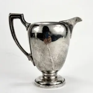 Silver pitcher with ornate handle and spout.