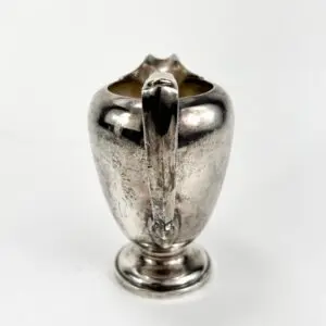 Silver creamer with ornate handle design.