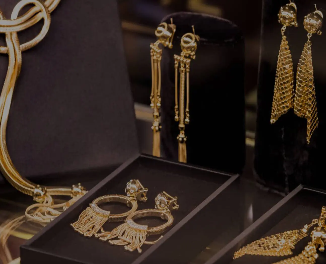 A collection of gold jewelry is displayed, including long dangle earrings and hoop earrings with tassels, set on a black velvet surface.